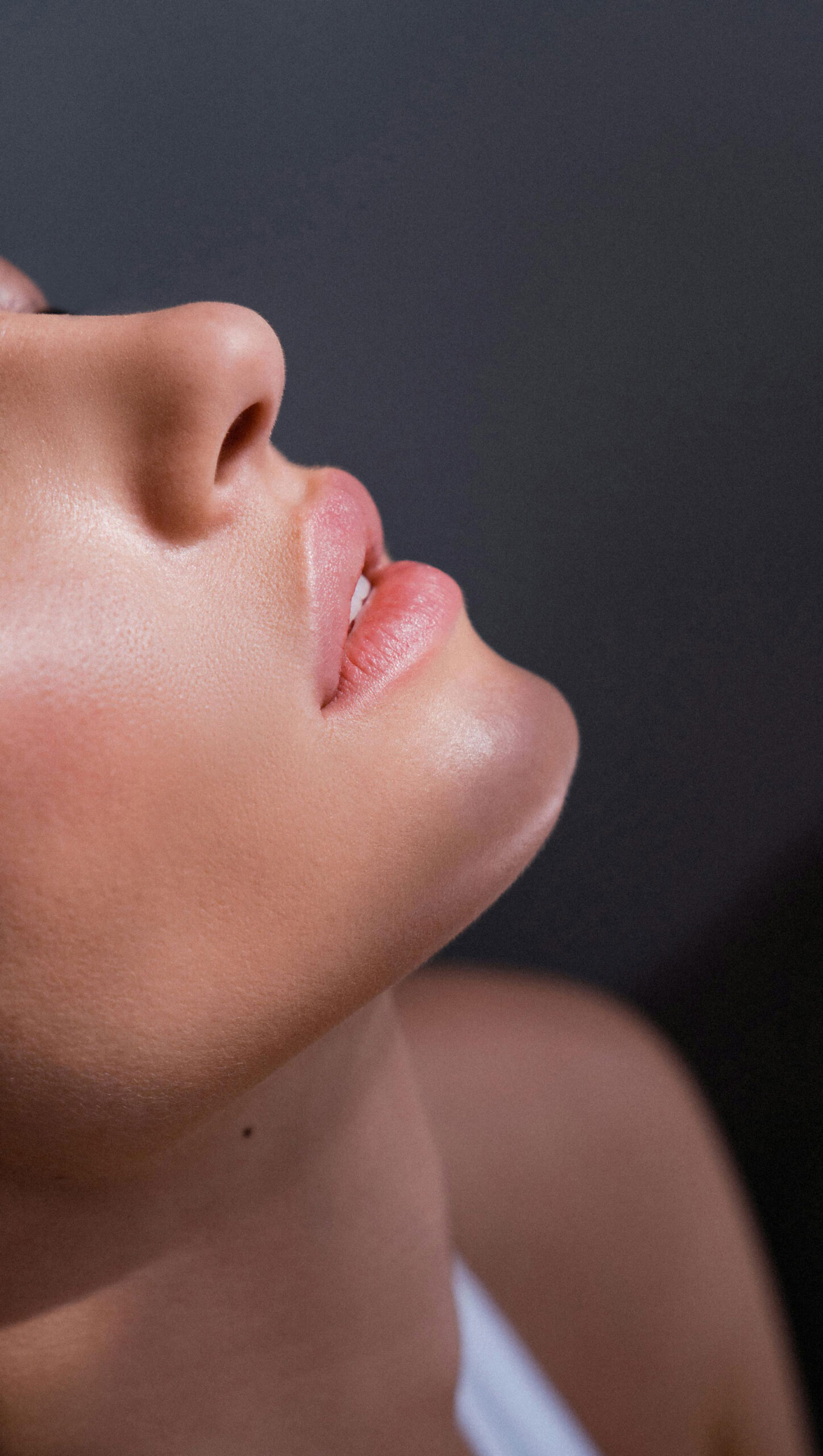 Close-up of a woman's side profile showing the nose and pink lips against a dark background.